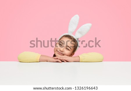 Cute content girl wearing bunny ears on headband and leaning on hands dreaming happily on white background 