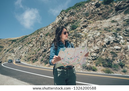 vintage photo female hiker pick up local paper map looking choosing travel destination at road trip on highway 1 california usa. confident girl backpacker in sunglasses walking on sunny day outdoor