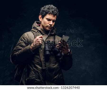 Serious traveler with binoculars looking into the phone on a black background