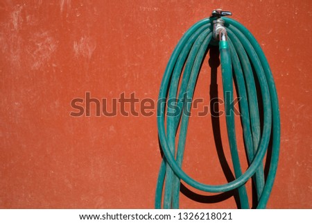 A hose hanged on a faucet on the colored wall