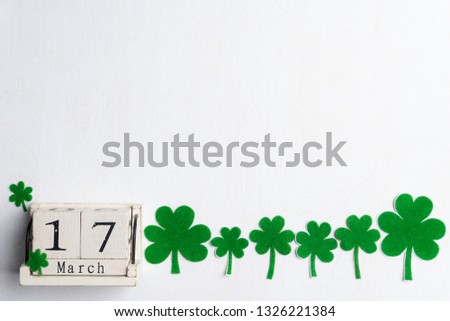 Block calendar for St Patrick's Day, March 17, with green clover leaf, green water and paper tag on white wooden background