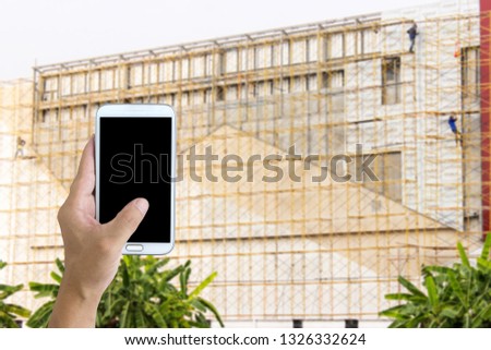 Man use mobile phone, blur image of steel truss structure in construction site as background.