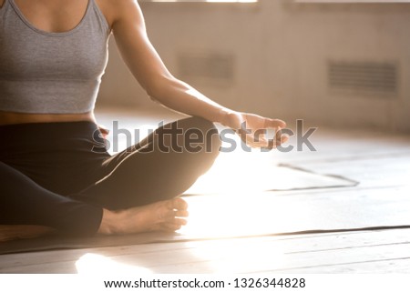 Young sporty yogi woman practicing yoga, doing Easy Seat exercise, Sukhasana pose, working out, wearing sportswear, black pants, top, indoor close up, yoga studio. Well being, wellness concept Royalty-Free Stock Photo #1326344828