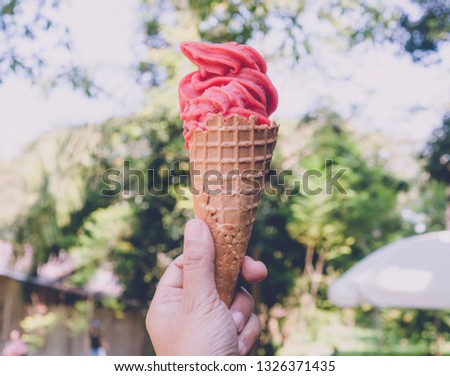 Hand holding ice cream cone with green garden background