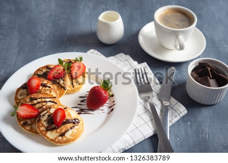 Homemade pancakes with strawberry and chocolate sauce with coffee on dark background. Breakfast, nutrition concept. Copy space. Side view.