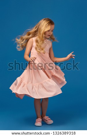 Fashionable little girl in a pink dress is posing on a blue background.