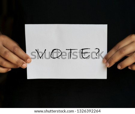 Male hand holding placard or ballot paper written vote for election vote concept isolated in black background. Voter in India.