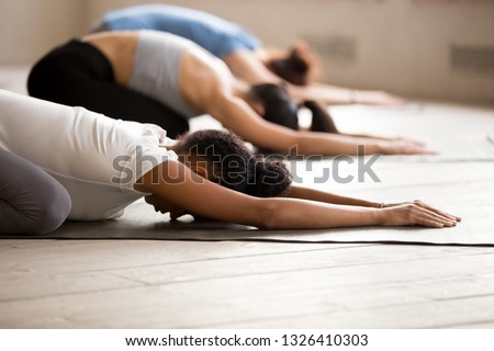 Group of diverse young sporty people practicing yoga, doing Child exercise, Balasana pose, working out indoor close up, mixed race female students training at club studio. Well being, wellness concept Royalty-Free Stock Photo #1326410303