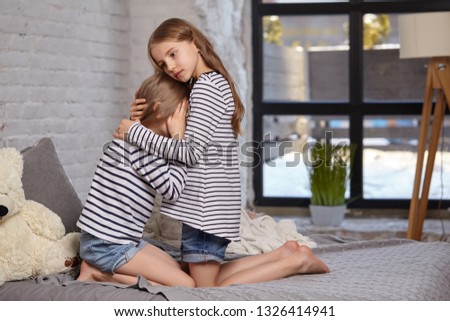 The image of two little sisters sitting on the bed in the room.