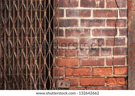 Cracked urban brick wall bordered by rusty metal has multiple patterns and textures for use as background.