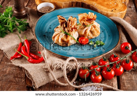 Pancakes with salmon, cream cheese and herbs. Bags tied with dill on a blue plate, next to the products for cooking,