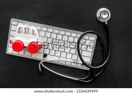 Call doctor online concept. Ambulance vehicle toy near computer keyboard and stethoscope on black background top view