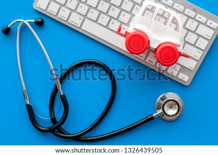 Call doctor online concept. Ambulance vehicle toy near computer keyboard and stethoscope on blue background top view