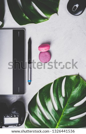 Close-up view of photographer's of graphic designer's workplace. Tablet, stylus, camera and zoom lens, optical wireless mouse, macarons, monstera green leaf