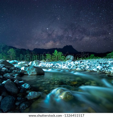 Water river flowing between rocks with milky way over Mount Kinabalu at Sabah Malaysia, North Borneo. Image contain grains, noise, soft focus and blur due to wide aperture, long exposure and high ISO.
