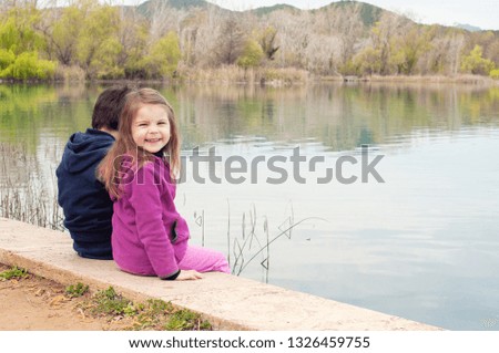 Children sit by the lake and admire in spring nature. Unity with nature.  Children relax outdoors. Freedom  and unity concept. 