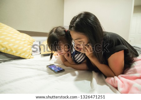 Asian women and girl with tan skin and happy feeling looking something at mobile phone on bed in the gray bedroom. Relax time in in the family concept.