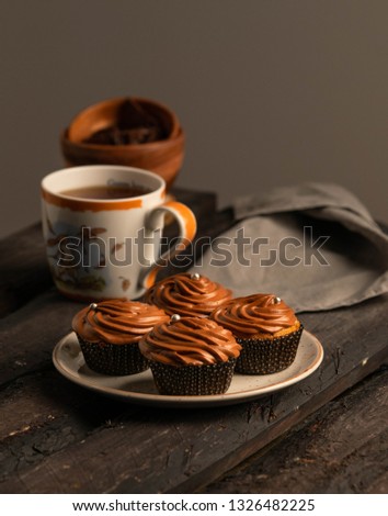 A dessert of chocolate cupcakes, on a dark wooden backdrop, dark background, on a rustic plate, cup of tea on background and  bowl with chocolate: CIRCA 03.2019-Moscow/Russia