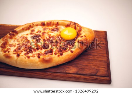 Yellow crispy adzharian khachapuri on a cooking paper on a wooden tray isolated at white background