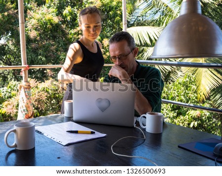 A multiethnic couple of freelancers working using laptop on green tropic background. Multiracial group of freelancers  working on a table in open doors office. Two coworkers in a team meeting. 