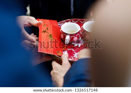 Wedding couple holding a tray with tea cups and red envelope packet/hongbao from eldest. Chinese Wedding with Double Happiness Text Calligraphy Illustration on red packet.