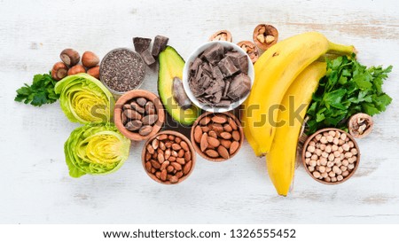 Foods containing natural magnesium. Mg: Chocolate, banana, cocoa, nuts, avocados, broccoli, almonds. Top view. On a white wooden background. Royalty-Free Stock Photo #1326555452