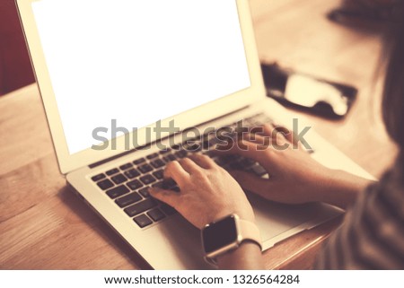 Mockup image of a woman using and typing on laptop with blank white screen on wooden table in modern cafe 