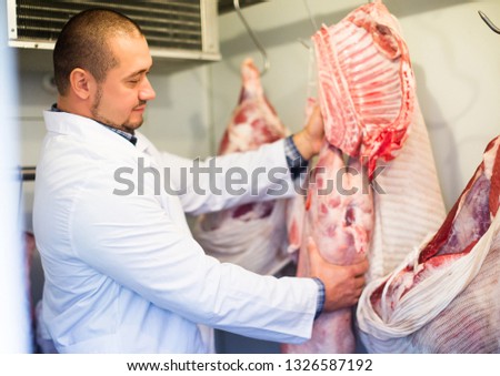 Adult butcher cutting fresh lamb meat in workshop