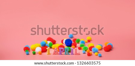 1 april date. April Fool's Day. creative minimal concept. Wooden letters "1 April" and fluffy colorful balls on pink background. 