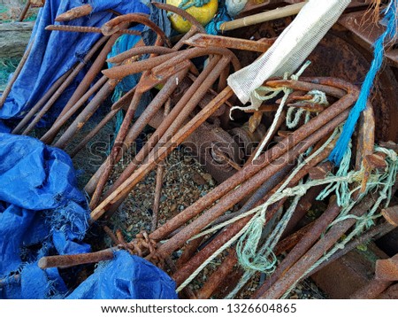 A pile of very old, rusty, small, fishing boat anchors pictured on a shingle fishing beach with strands of coloured rope