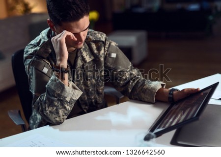 Nostalgic American soldier looking at national flag in picture frame while being far away from home.