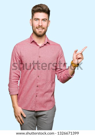 Young handsome business casual man with a big smile on face, pointing with hand and finger to the side looking at the camera.