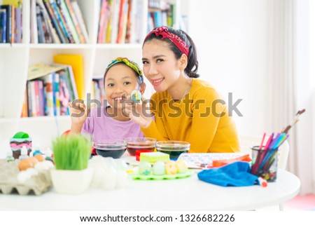 Picture of cute little girl and her mother showing a painted Easter egg while sitting at home