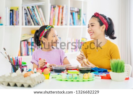 Picture of cute little girl and her mother decorating Easter eggs with liquid dye at home