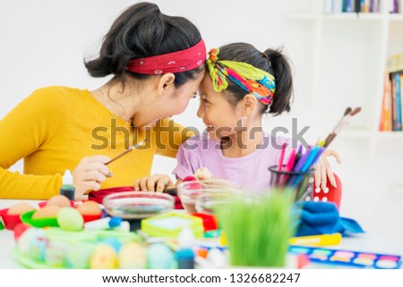 Picture of happy woman and her daughter painting eggs while doing preparation for Easter at home