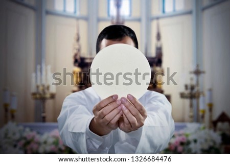 Picture of pastor celebrating a mass while holding a sacramental bread in the church