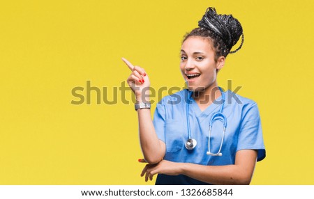 Young braided hair african american girl professional surgeon over isolated background with a big smile on face, pointing with hand and finger to the side looking at the camera.