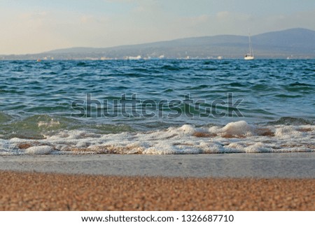 white foam from the blue sea wave on a sandy beach with mountains in the background on a Sunny day on November 25 in Gelendzhikn November 25 in Gelendzhik