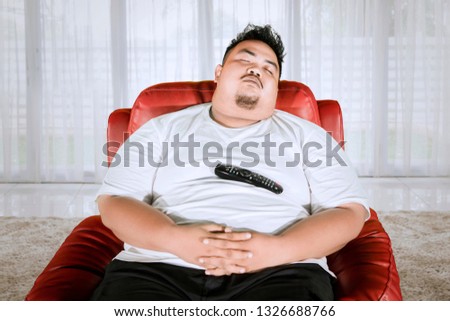Picture of an Asian obese man taking a nap on the sofa during watching television in the living room