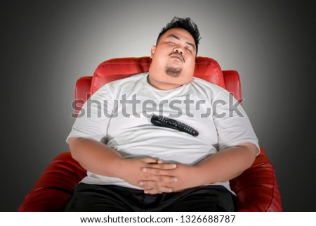 Picture of Asian fat man sleeping on the armchair while watching TV in the dark room