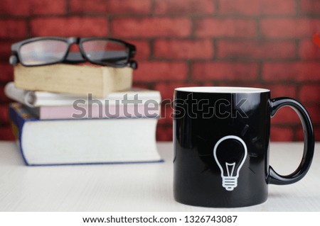Black mug with bulb idea sign and books with background. Selectively focused and isolated for conceptual photo.