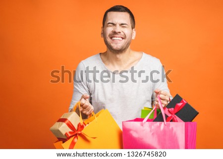 It's shopping time! Happy young man with colorful paper bags isolated on orange background.