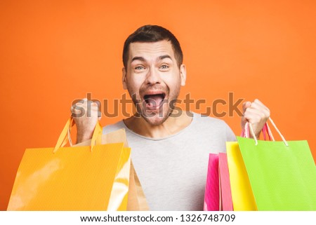 It's shopping time! Happy young man with colorful paper bags isolated on orange background.