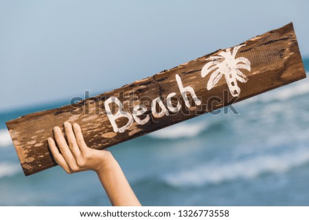 Female hand holding old wooden sign with lettering "Beach"
