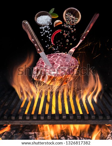 Raw Steak ribeye cooking. Conceptual picture. Steak with spices and cutlery under burning grill grate.