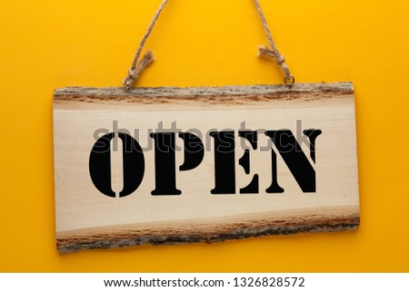 Open word on wooden sign hanging on a rope on yellow background.