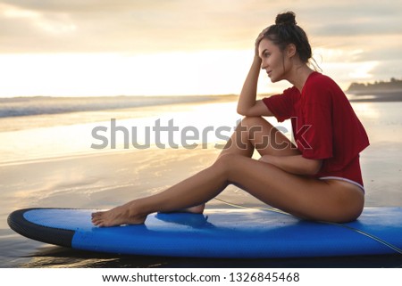 Young woman sitting on surfboard on the beach after her surfing session