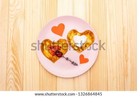 Heart shaped pancakes for romantic breakfast with strawberry jam, silver spoon and paper hearts. Shrovetide (carnival) concept. On wooden background, top view.
