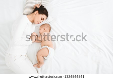 Mother and child connection. Young woman sleeping and touching her baby's hand, top view with free space