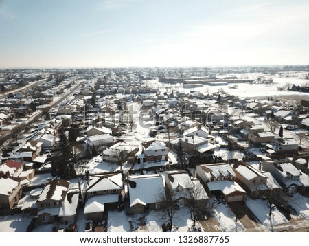 Aerial drone photo, top down, of suburban houses in Canada everything is white and covered with snow in the sunshine.